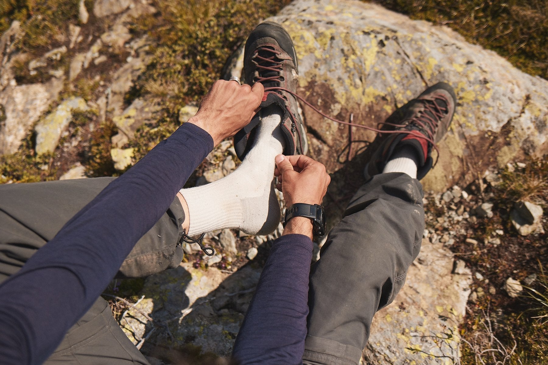 Hiker tightening hiking boots over merino wool socks on a rocky mountain trail