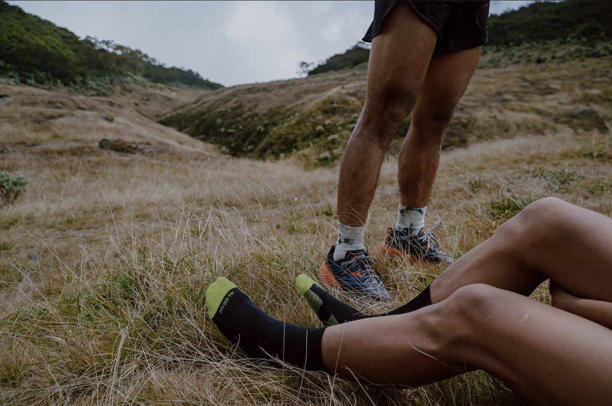 Two hikers wearing merino wool crew socks and quarter socks side by side on a grassy trail