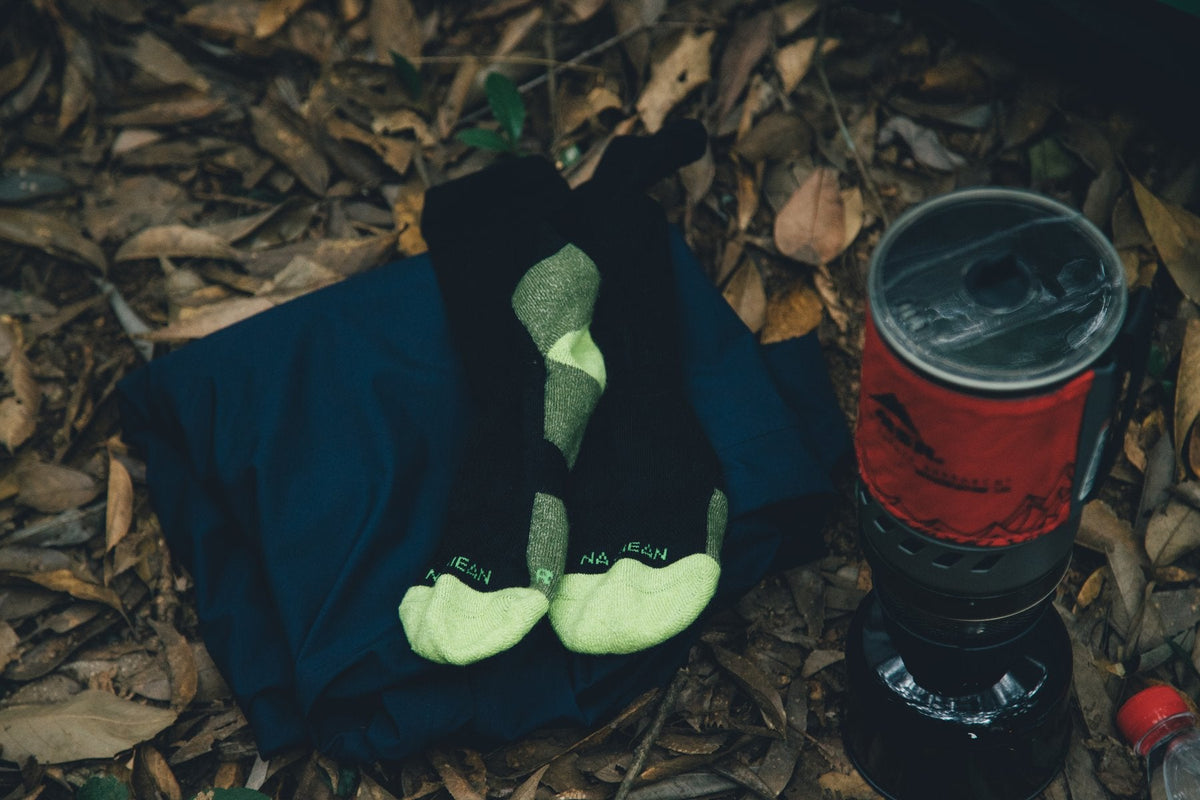 Merino wool socks laid out beside a camp stove on fallen leaves