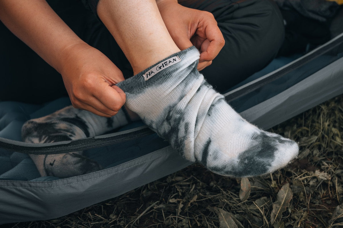 Hiker pulling on a tie-dye merino wool sock at a campsite
