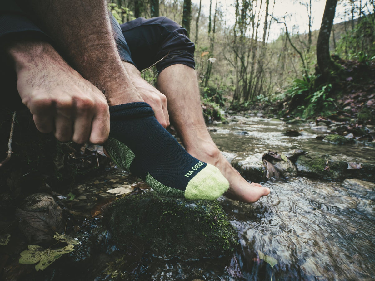 Pulling on a merino wool hiking sock beside a forest stream